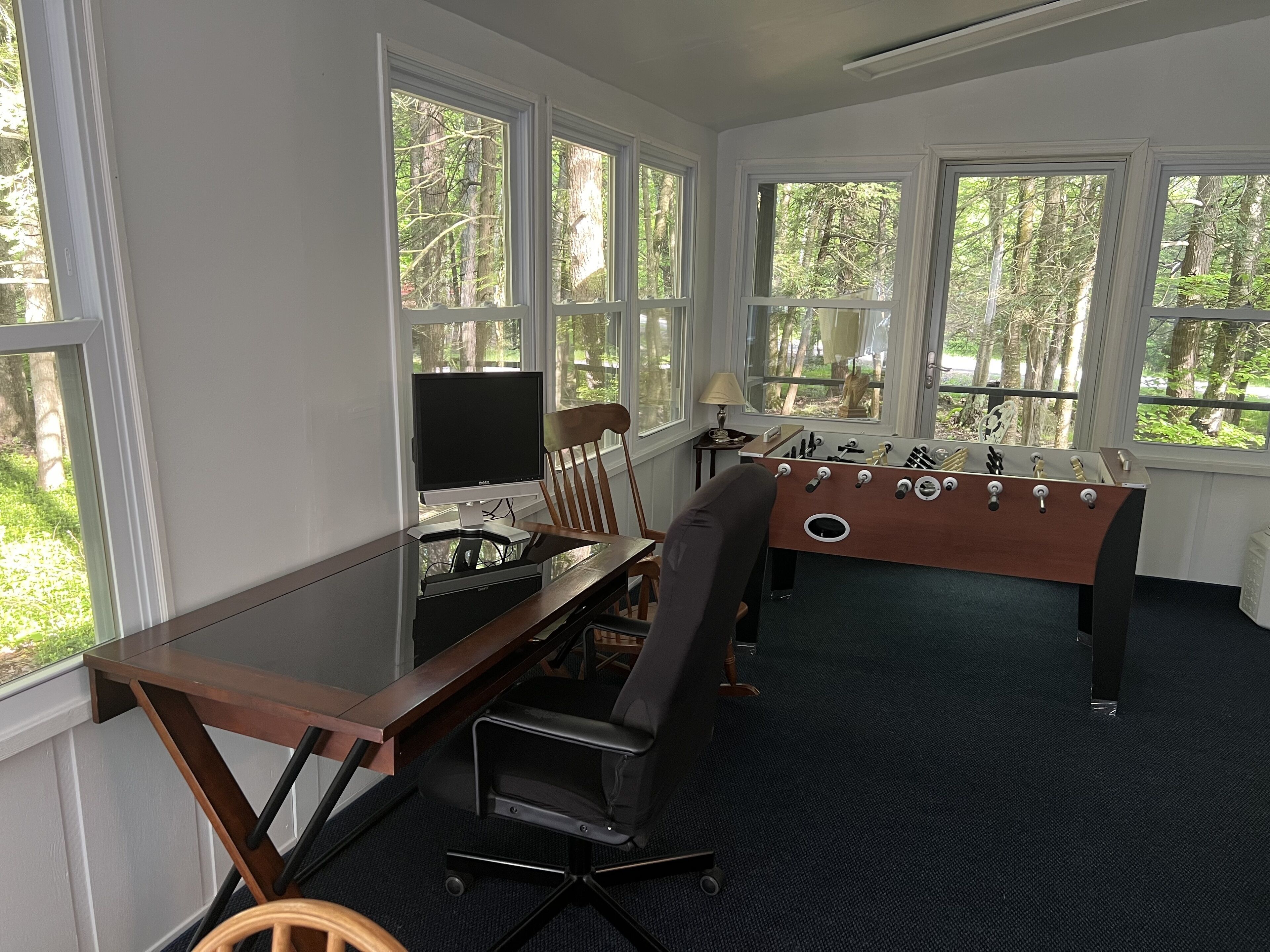 A room with a wooden desk, a computer, a chair, and a foosball table.