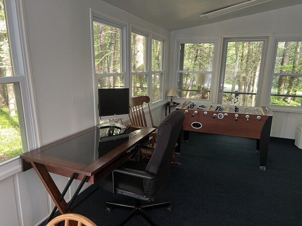 A room with a wooden desk, a computer, a chair, and a foosball table.