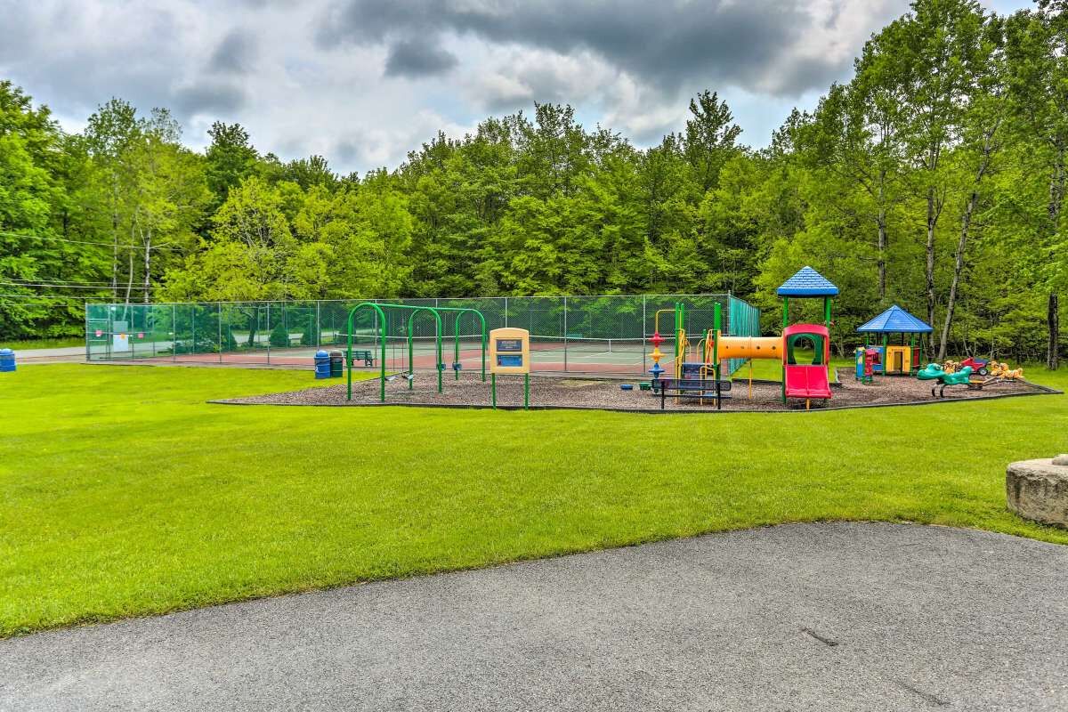 A playground with various play structures, surrounded by a fenced area and a grassy field.