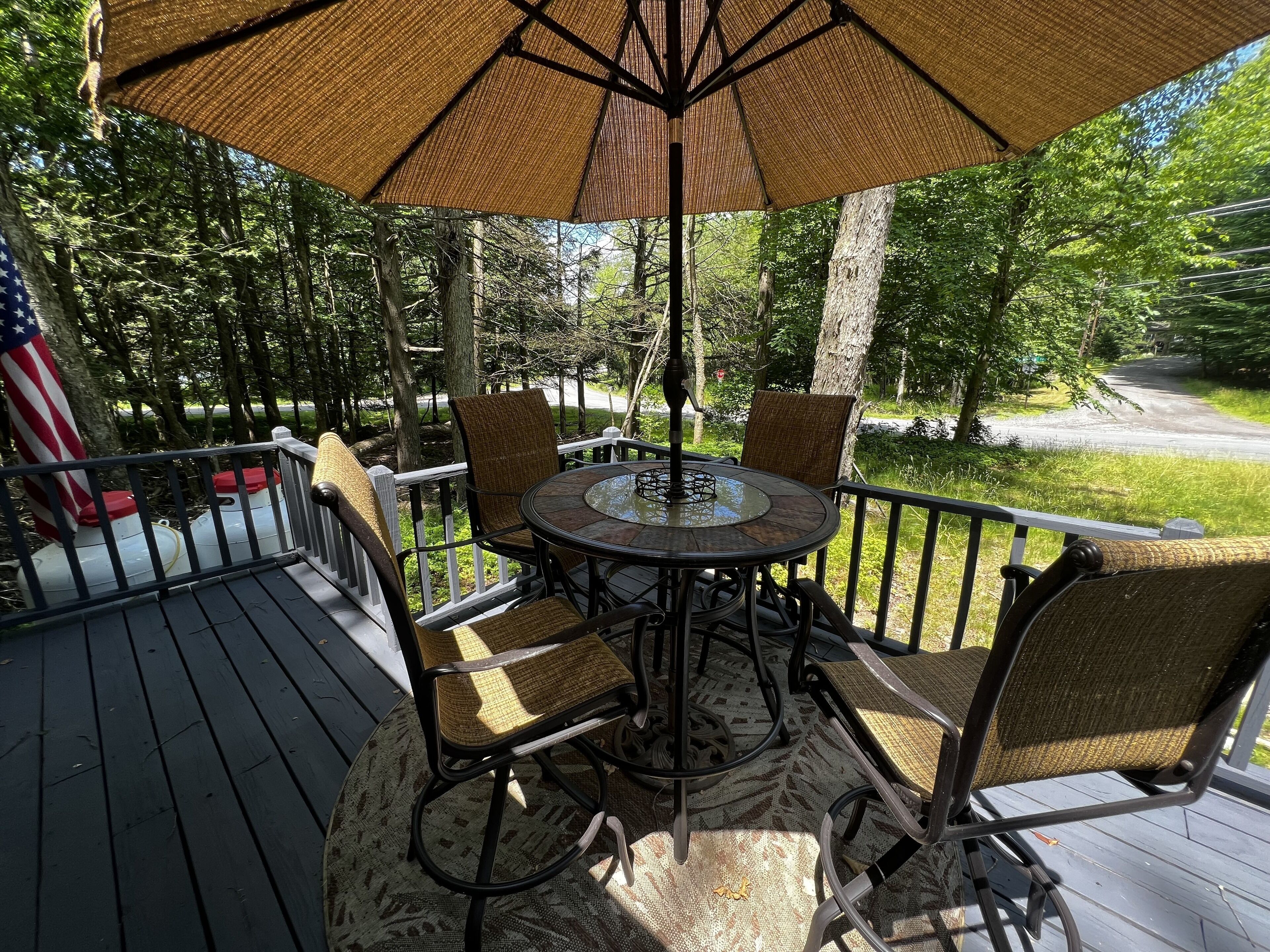 Une terrasse avec une table ronde et quatre chaises, un drapeau américain et un grand parasol.
