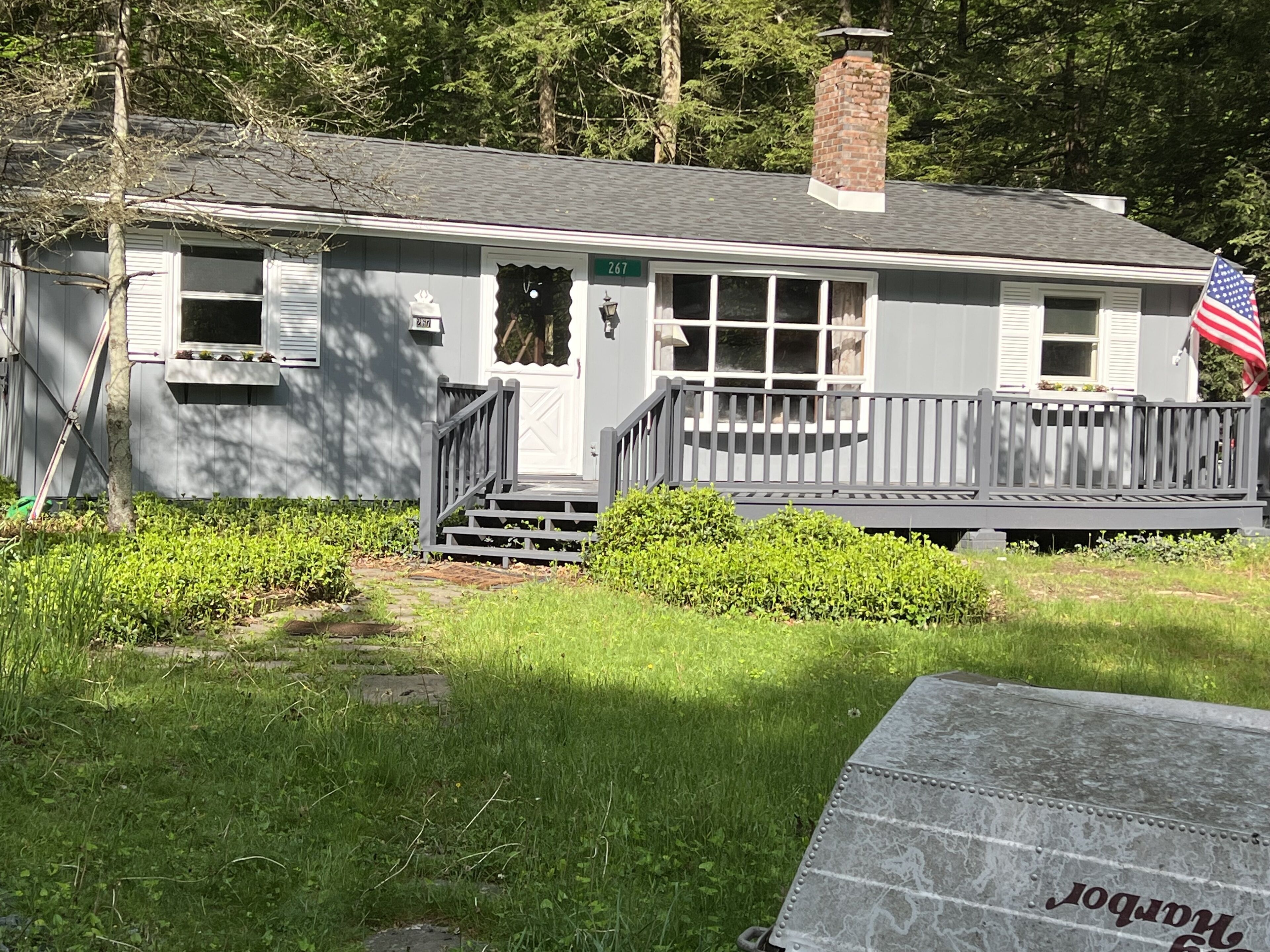 A single-story house with a front porch, a chimney, and an American flag.