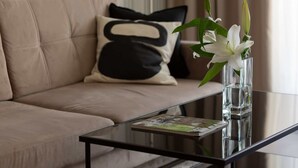 A modern living room with a glass coffee table, a beige sofa, and a decorative vase with white flowers.