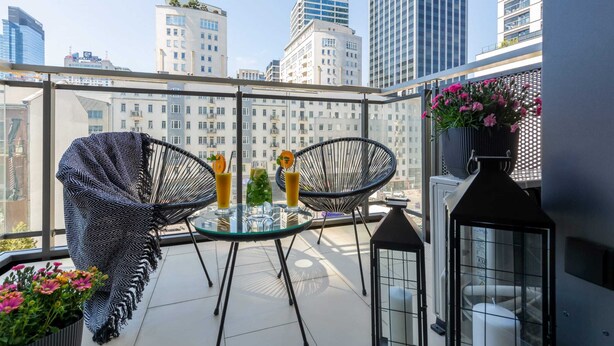 A balcony with two wicker chairs, a glass table with drinks, and a potted plant.
