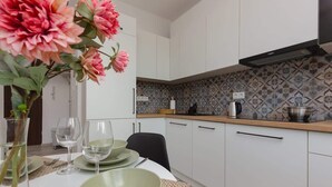 Una cocina moderna con armarios blancos, salpicadero estampado y una zona de comedor con platos verdes y copas de vino.