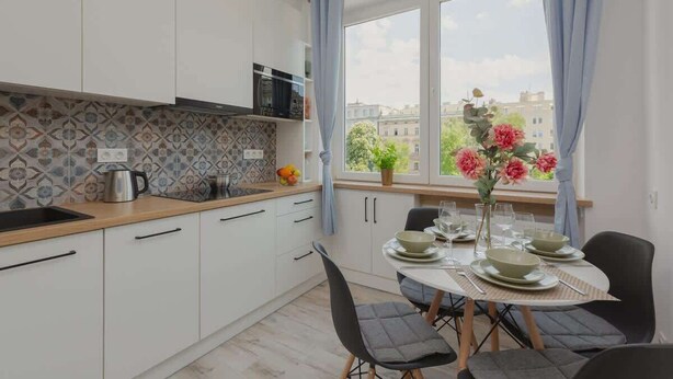 Una cocina moderna con armarios blancos, encimera de madera y un área de comedor con una mesa lista para dos comensales.