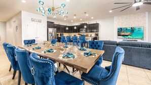 A modern dining area with a wooden table, blue upholstered chairs, and a chandelier. - Two Villas Two Resorts Two Blocks Apart Sleeps 41 (Kissimmee)