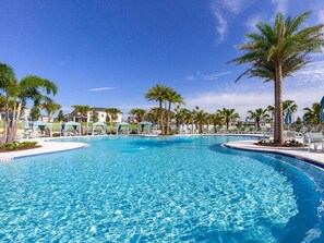 Una piscina amplia y cristalina rodeada de palmeras y sillas de descanso, bajo un cielo azul despejado.