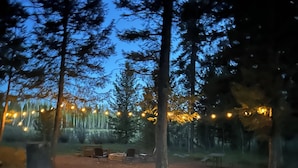 Un terrain de camping avec des tentes et des arbres, des guirlandes lumineuses et un sol en terre.