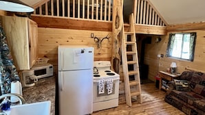 L’intérieur de la cabane comprend un coin cuisine équipé d’un réfrigérateur, d’une cuisinière et d’un four à micro-ondes. Une échelle en bois mène à une mezzanine aménagée en espace de couchage.