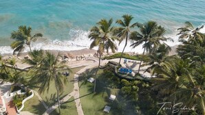 Luchtbeeld van een resort met een strand, palmbomen en een zwembad.