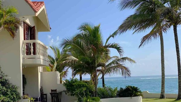 Een pand aan het strand met een balkon, palmbomen en uitzicht op de oceaan.
