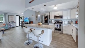 Une cuisine moderne avec des armoires blanches, un grand îlot central doté de tabourets de bar, des appareils en acier inoxydable et une batte de baseball en bois suspendue au plafond.