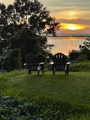 Dos sillas Adirondack mirando un cuerpo de agua con un atardecer de fondo.
