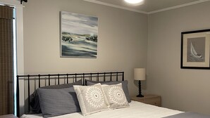 A bedroom with a bed, a ceiling fan, a nightstand, a lamp, and two framed pictures on the wall. - DAPHNE SCENIC BAY VIEW CONDO (Daphne)