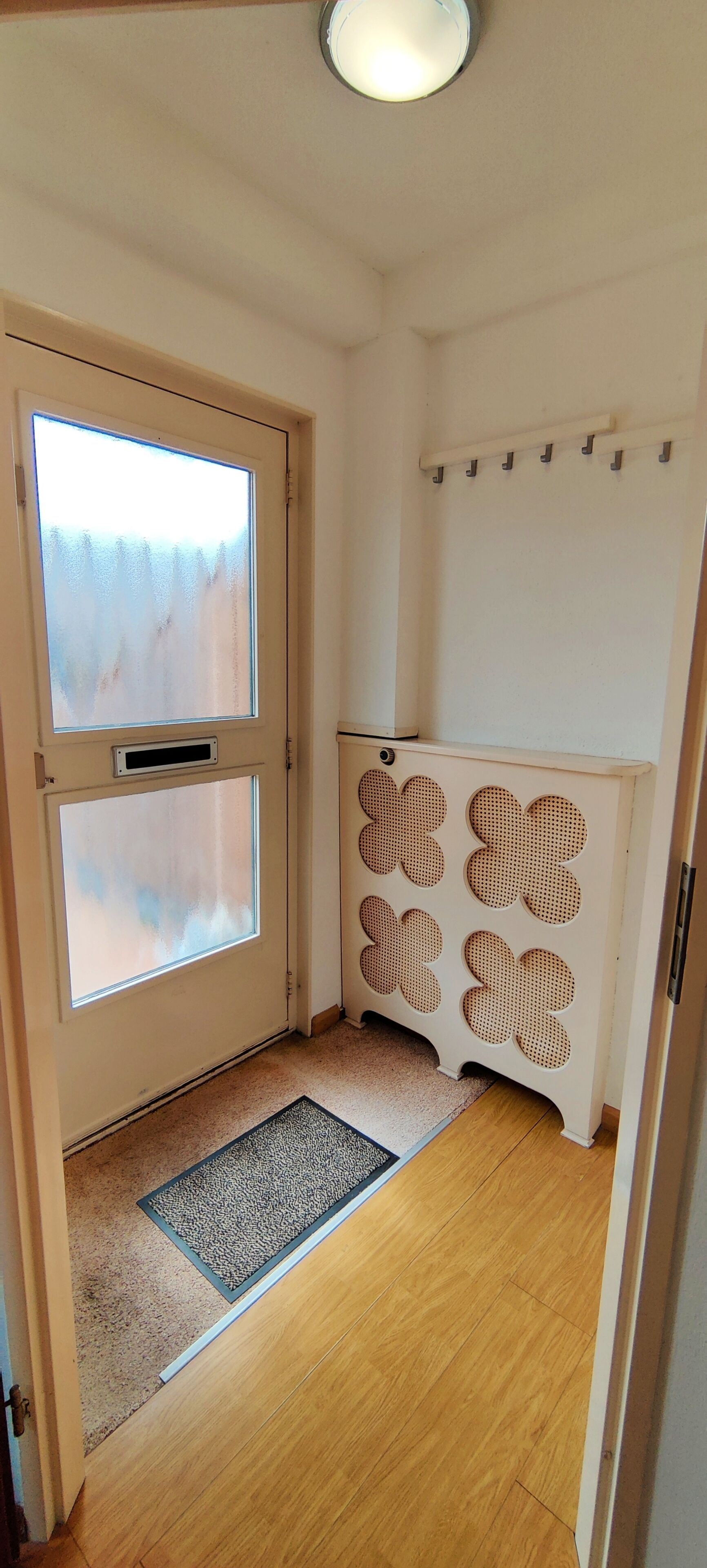 Une pièce dotée d’un plancher en bois, d’une porte avec des panneaux en verre dépoli, d’un radiateur orné d’un panneau décoratif et d’un luminaire fixé au plafond.