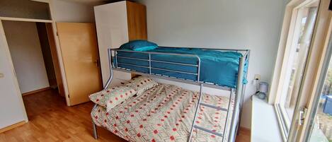 A bunk bed with a patterned blanket, a wardrobe, and a window.