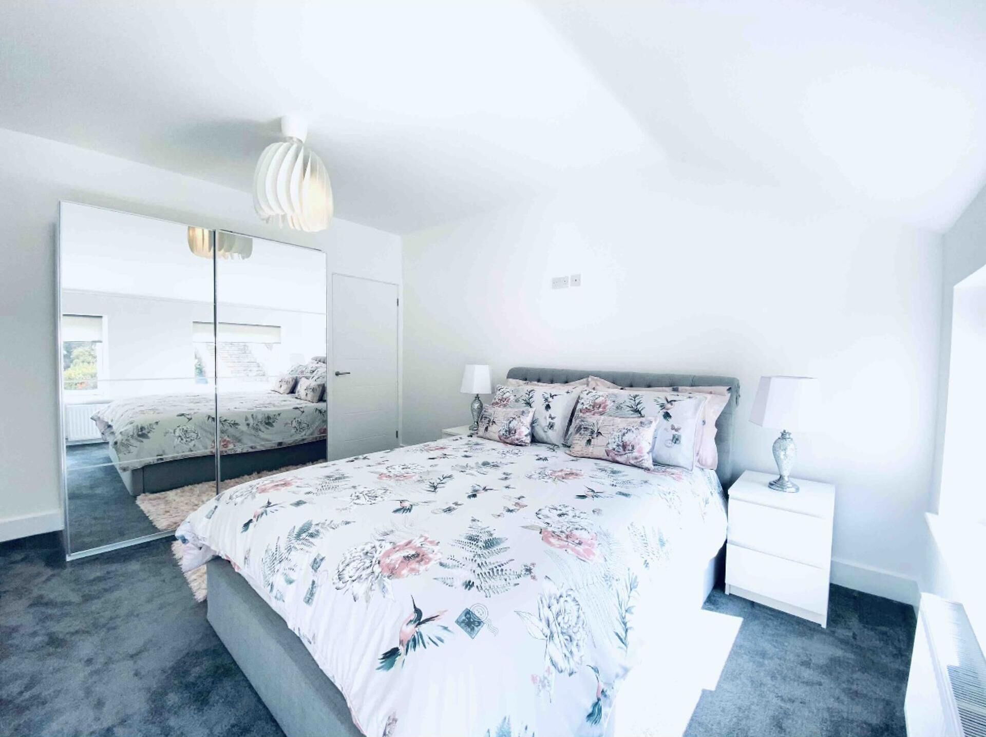A modern bedroom with a large bed, a mirror, and a nightstand.