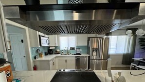 Una cucina moderna con piano cottura a induzione nero, elettrodomestici in acciaio inossidabile e un piano di lavoro in marmo bianco.