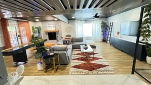 Un soggiorno moderno con un divano grigio, un tavolino da caffè e un tappeto decorato. Si nota un camino, una TV e una pianta nella stanza.