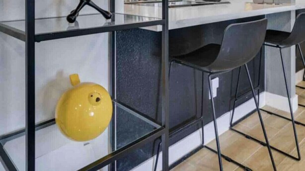Una cucina moderna con isola centrale, sedie nere e un elemento decorativo giallo su ripiano inferiore.