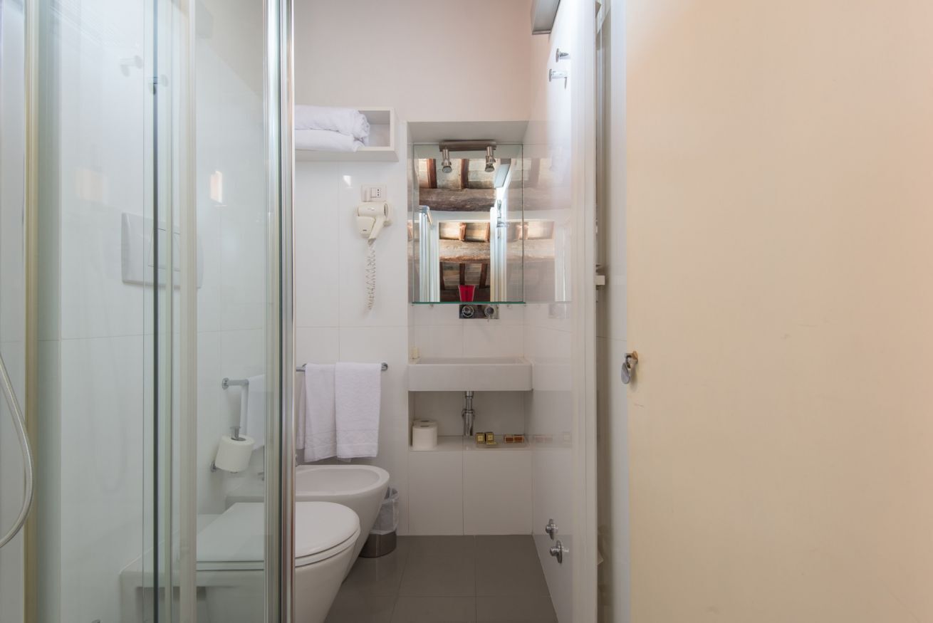 Ein kleines Badezimmer mit Duschkabine aus Glas, Toilette, Waschbecken mit Spiegel und Handtuchhalter.