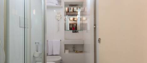 Ein kleines Badezimmer mit Duschkabine aus Glas, Toilette, Waschbecken mit Spiegel und Handtuchhalter.