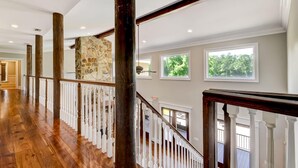 A spacious hallway with wooden flooring, white railings, and large windows offering views of greenery. - Luxury 7 bedroom mansion with horses, pool, hot tub, pond, swings and fire pit!  (Waverly)