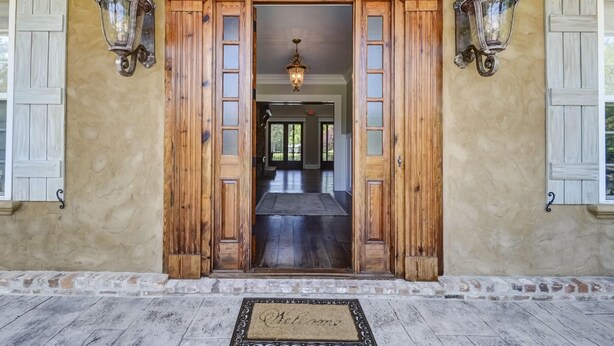 A wooden entrance with a welcome mat, two wall-mounted lanterns, and a view into a hallway. - Luxury 7 bedroom mansion with horses, pool, hot tub, pond, swings and fire pit!  (Waverly)