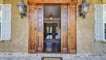 Une porte d’entrée en bois, un paillasson, deux lanternes fixées au mur et une vue sur un couloir.