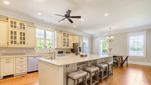A spacious kitchen with white cabinetry, a central island with stools, a ceiling fan, and a dining area with a chandelier. - Luxury 7 bedroom mansion with horses, pool, hot tub, pond, swings and fire pit!  (Waverly)