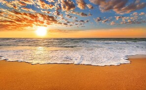 A beach with waves, a sunset, and a clear sky.