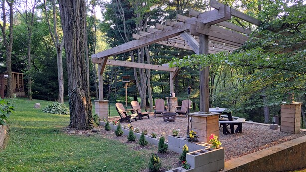 A wooden pergola with seating and a fire pit in a garden setting.