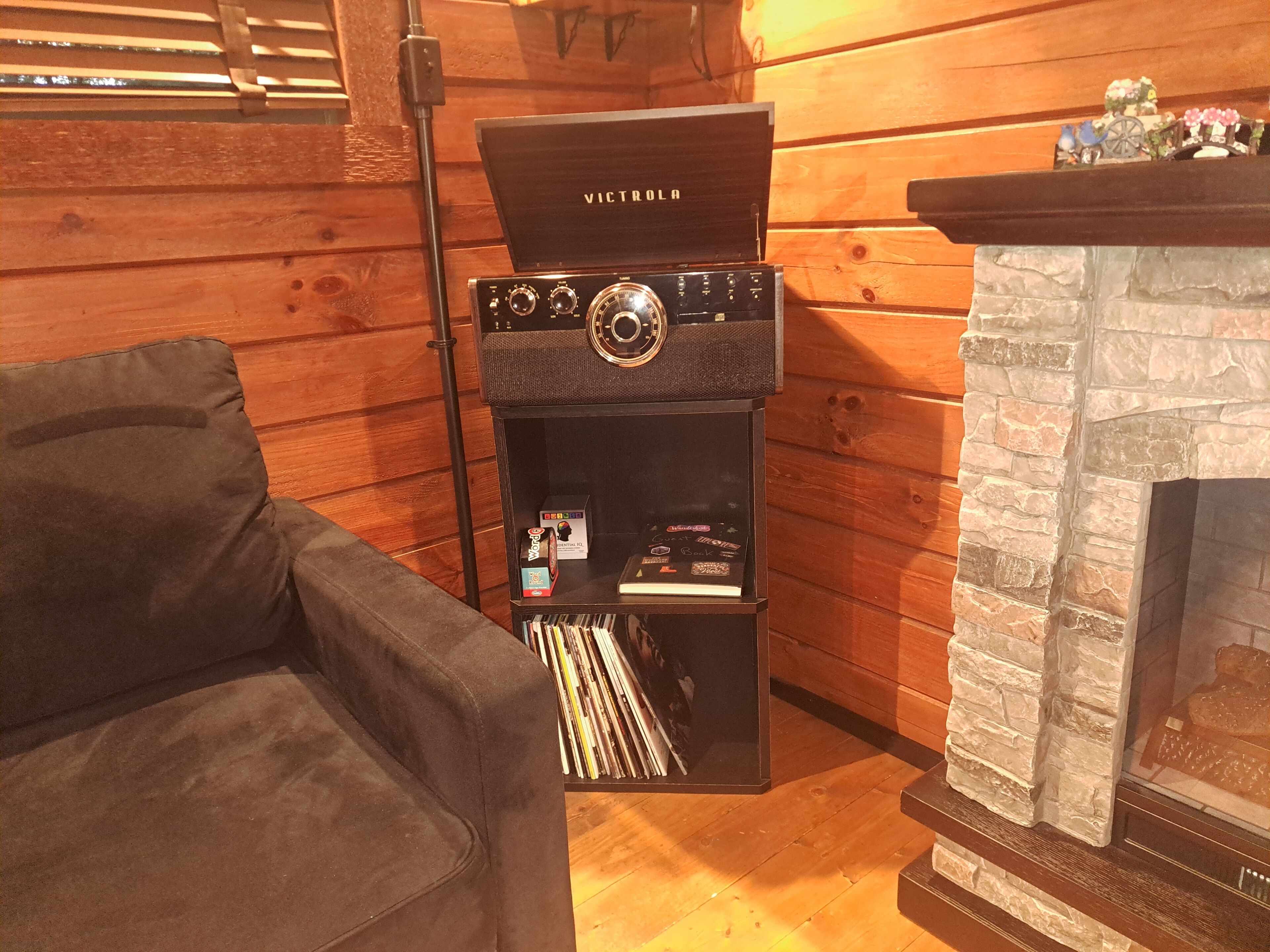 Een knus vertrek met een open haard, een houten wand, een zwarte speaker en een bank.