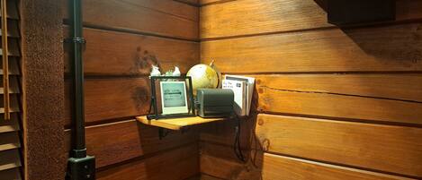 A corner of a room with wooden paneling, a shelf with books, a globe, a framed sign, and a tripod.