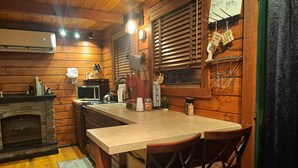 A cozy kitchen with wooden walls, a stone fireplace, a microwave, and a sink. There are two chairs and a table.