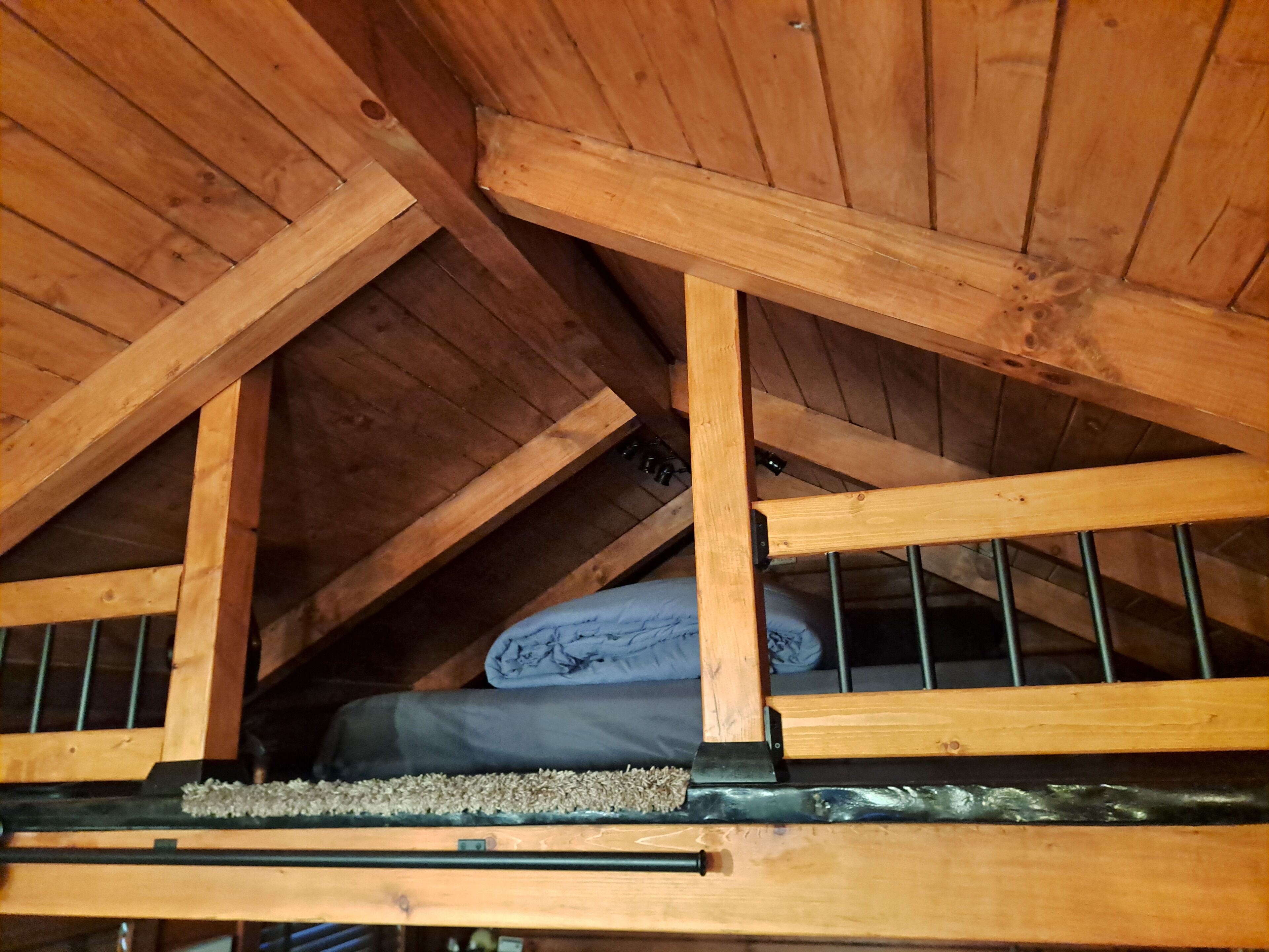 Una camera mansardata in legno con un letto a castello, un materasso e una coperta arrotolata.