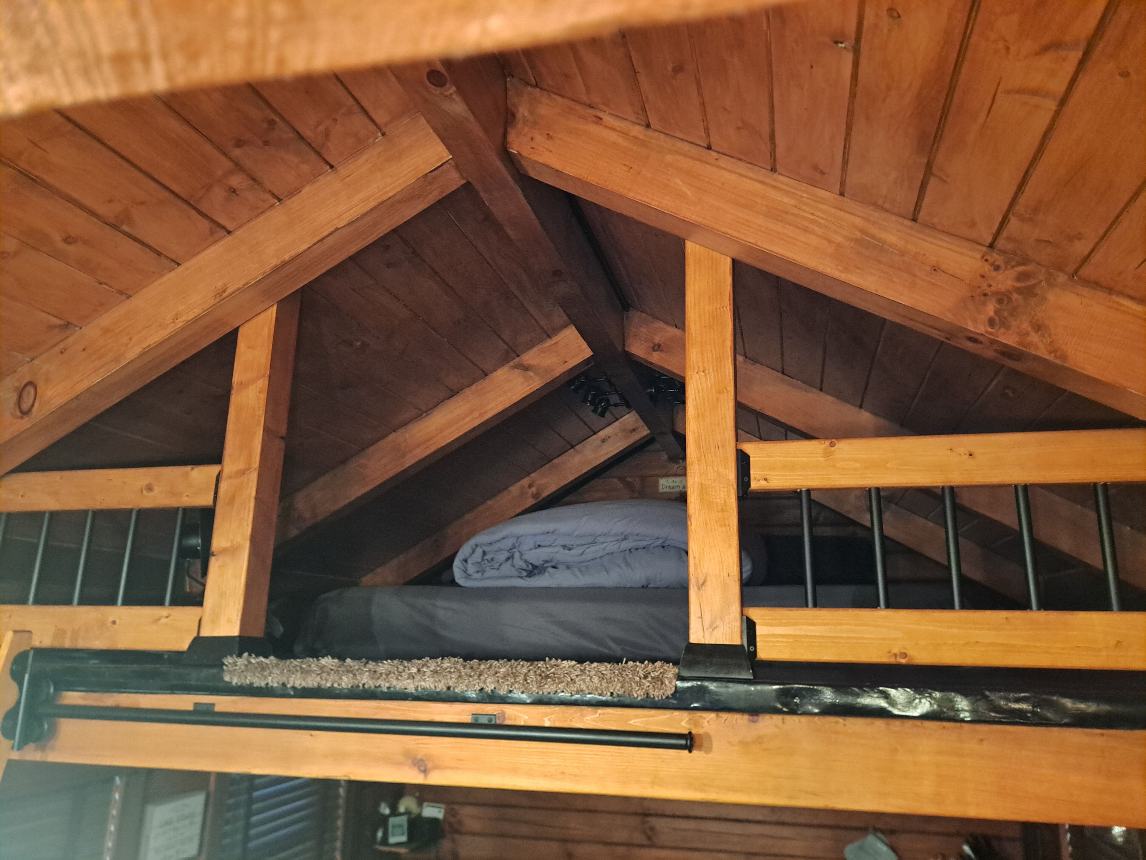 A wooden attic bedroom with a sloped ceiling, a metal railing, and a mattress on the floor.