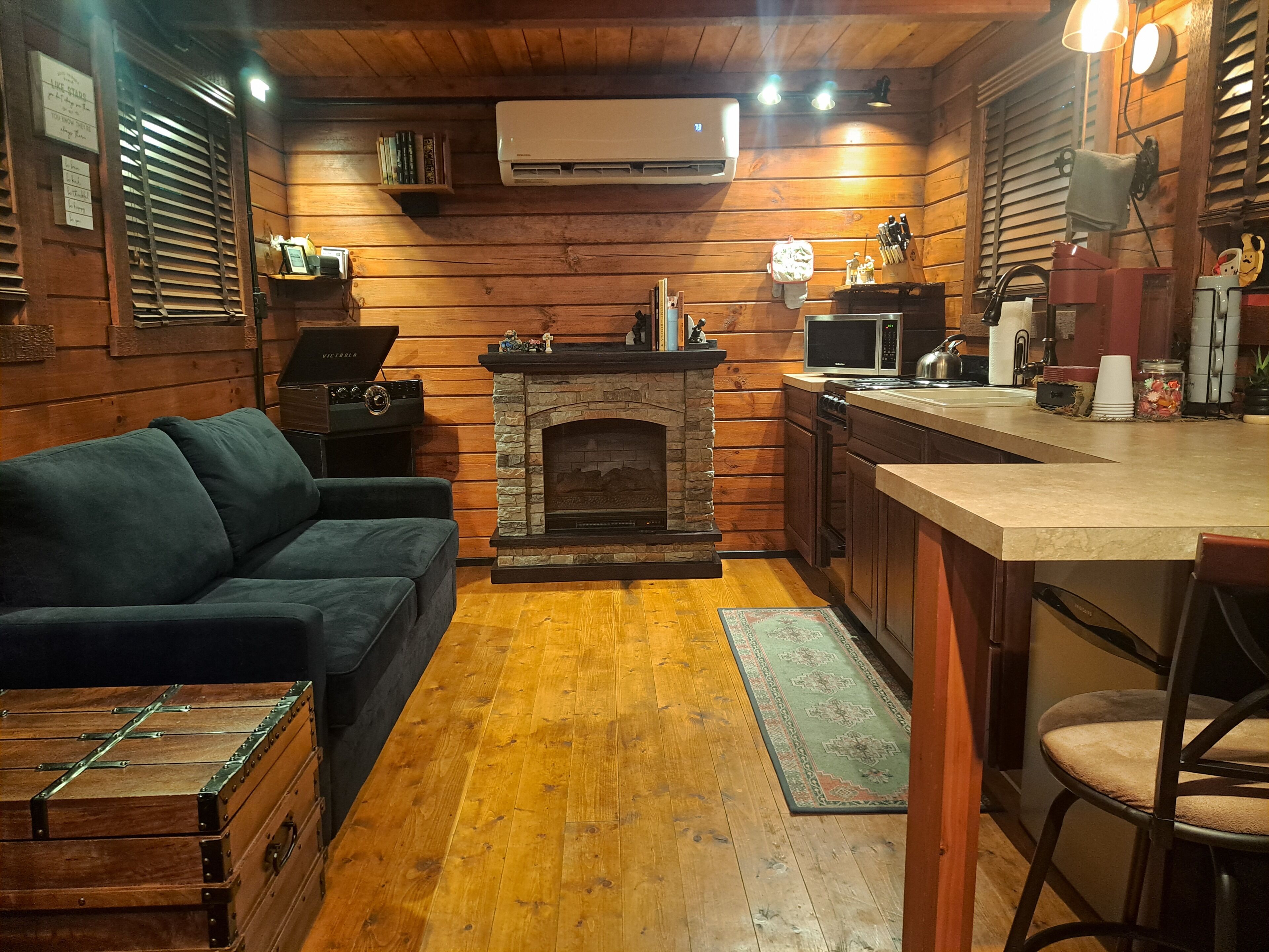 Een knus kamer in chaletstijl met een stenen openhaard, houten wanden, een bank, een zithoek en een kitchenette.