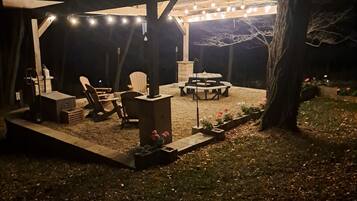 An outdoor patio area with a covered seating area, string lights, and a fire pit.