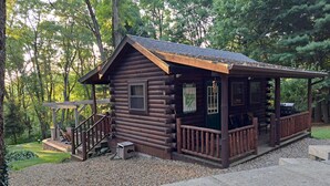 A rustic log cabin with a porch, a small deck, and a gravel driveway.