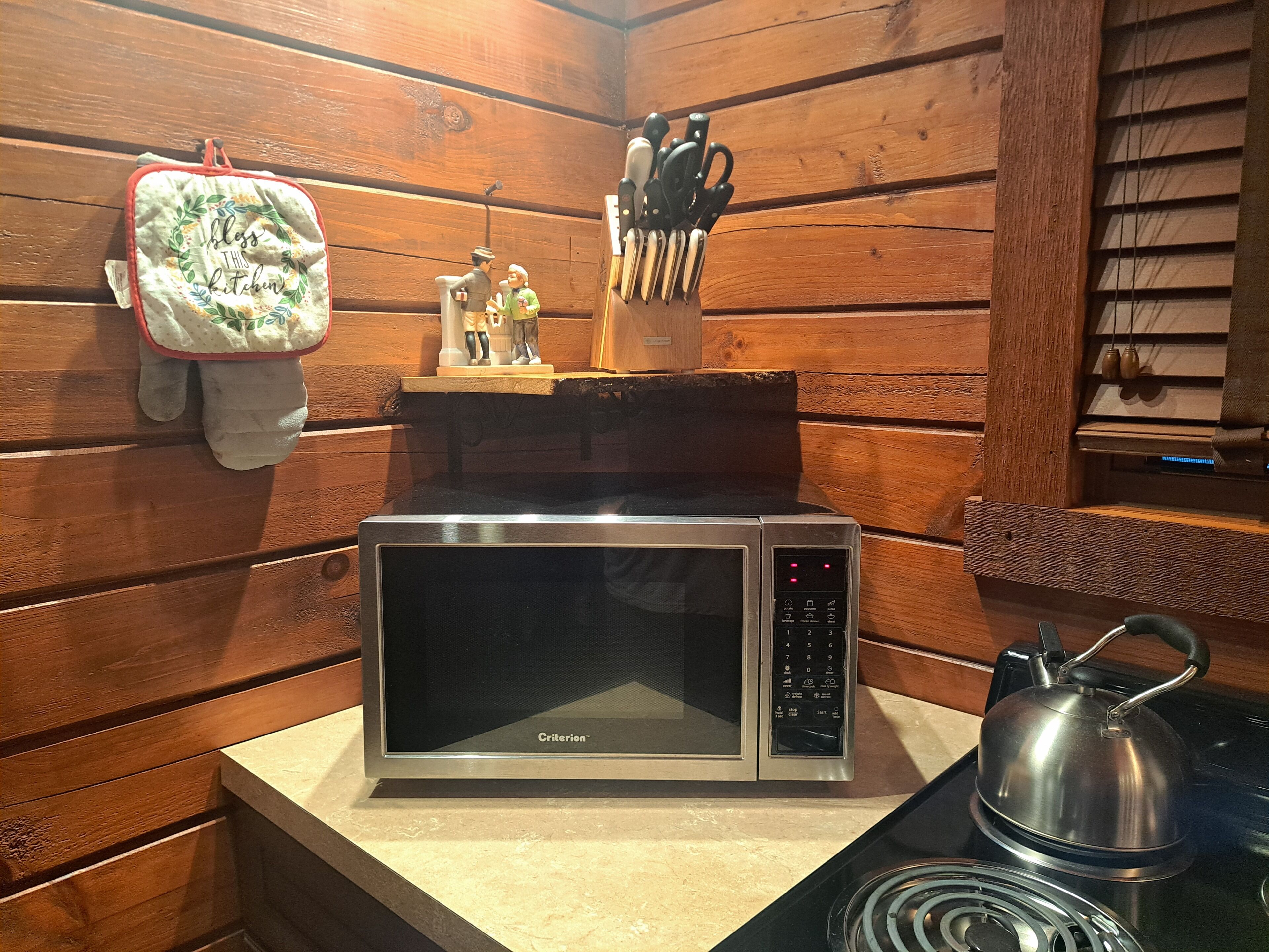 A kitchen with a stainless steel microwave oven, a kettle, and a set of knives on a wooden countertop.
