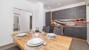 Een moderne eetruimte met een houten tafel voor vier personen, grijze kasten en een keuken met een bijzondere achterwand.