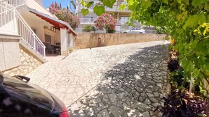 Een straat met cobblestones, met een auto aan de linkerkant, een gebouw met een trap en een balkon met roze bloemen.