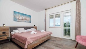 Een slaapkamer met een bed, nachtkastje, kapstok, een roze stoel en een raam met gordijnen.
