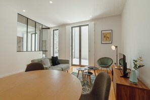 A modern living room with a large wooden table, a sofa, a green armchair, and a small coffee table. There is a sliding glass door leading to an outdoor area.