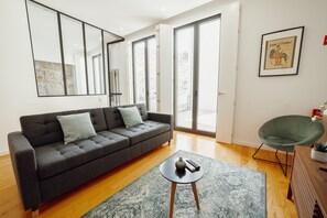 Un salon moderne avec un canapé gris, une petite table ronde sur laquelle se trouve une télécommande, et un fauteuil vert.