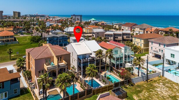 A coastal residential area with a prominent red location marker, featuring a central building with a swimming pool, surrounded by other residential buildings and palm trees. - Padre Parade • Private Heated Pool • 90-Second Walk to Beach (South Padre Island)
