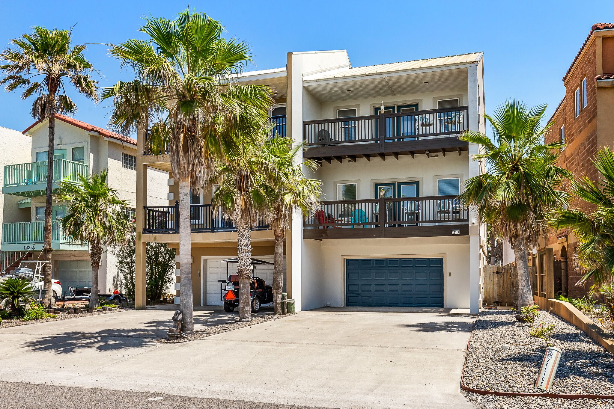 A multi-story residential building with a garage, palm trees, and a clear blue sky.
