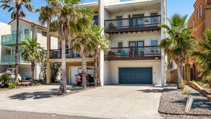 A multi-story residential building with a garage, palm trees, and a clear blue sky. - Padre Parade • Private Heated Pool • 90-Second Walk to Beach (South Padre Island)