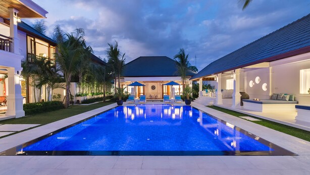 A modern pool area with a clear blue pool, surrounded by well-maintained greenery and a two-story building with large windows. - Villa Windu Asri (Seminyak)